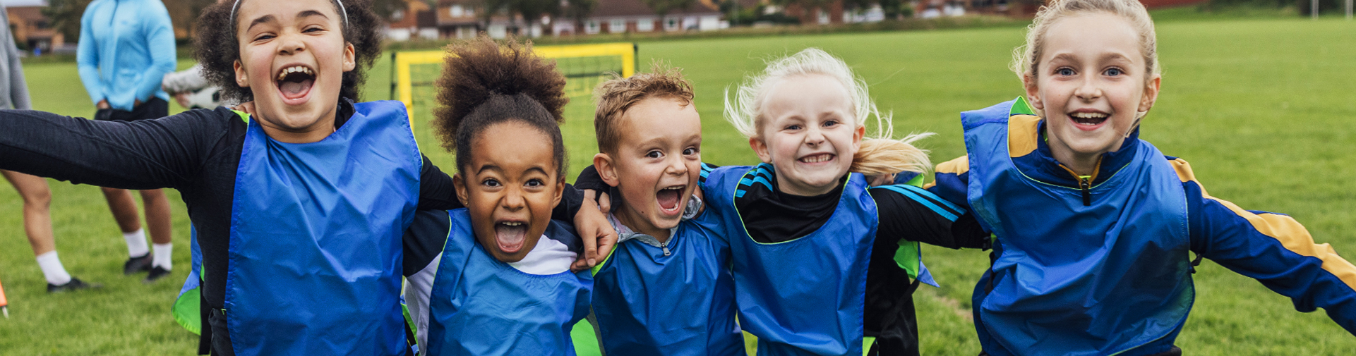 Smiling children in sports pinnies celebrating together on a field